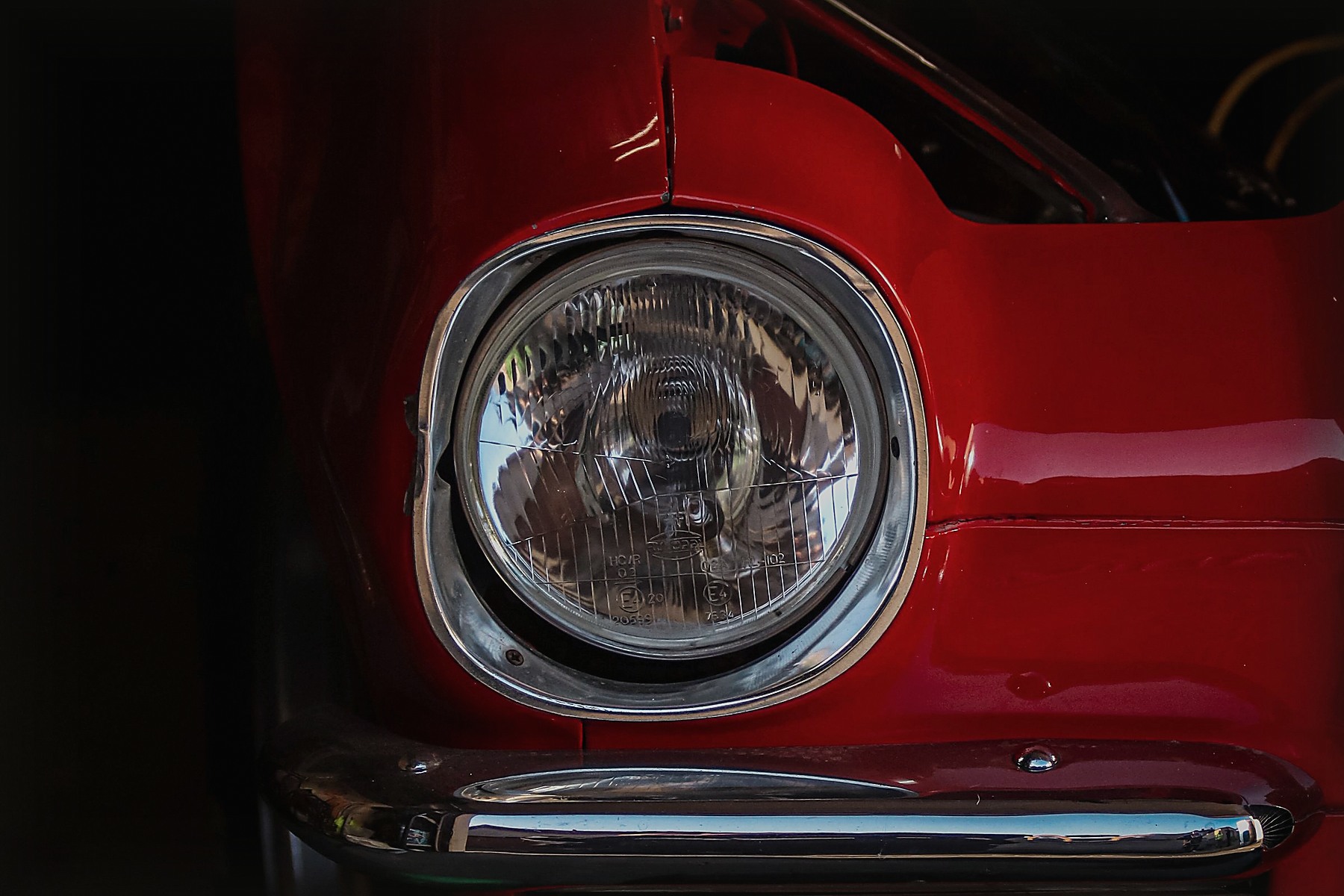 Close view of a red classic car headlight and chrome bumper
