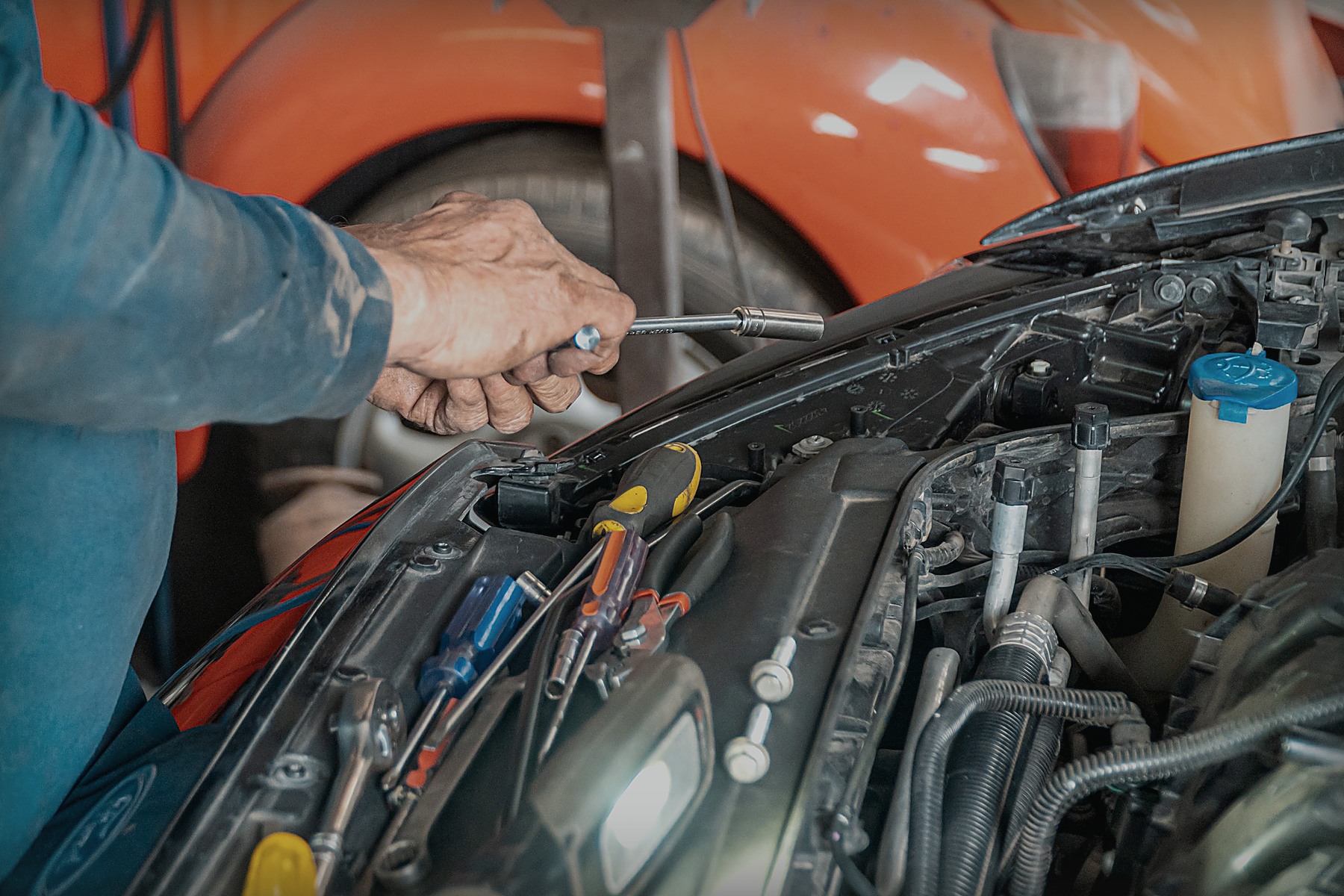 Mechanic holding a hand tool beside a vehicle