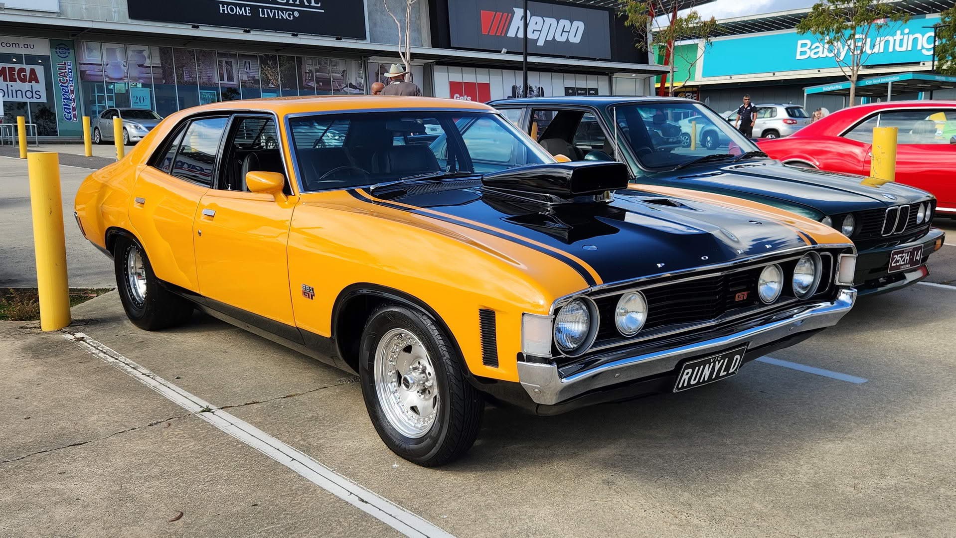 Orange Ford XA with a black bonnet and chrome grille at a car show