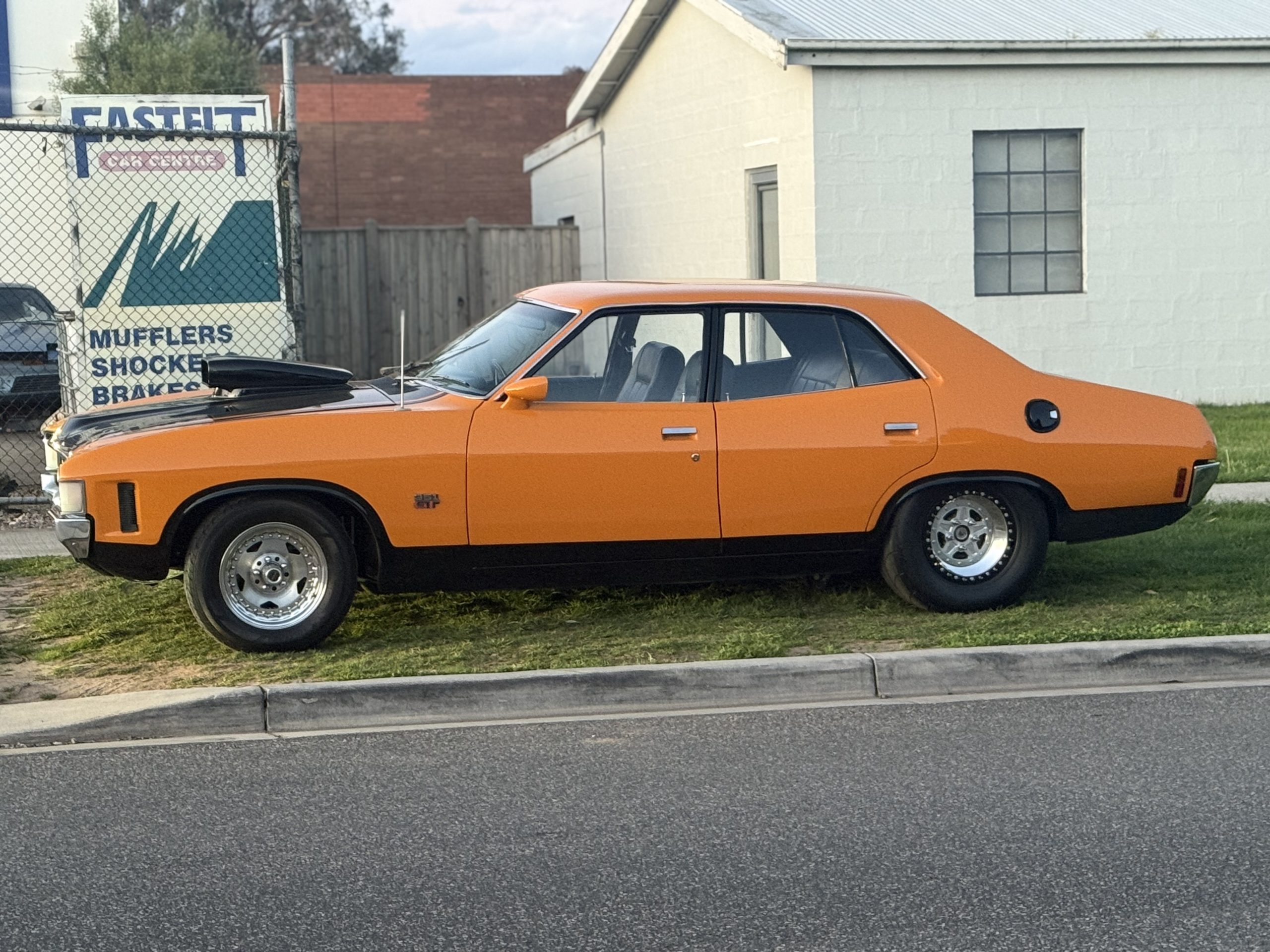 Side profile of an orange Ford XA with a black bonnet and chrome wheels